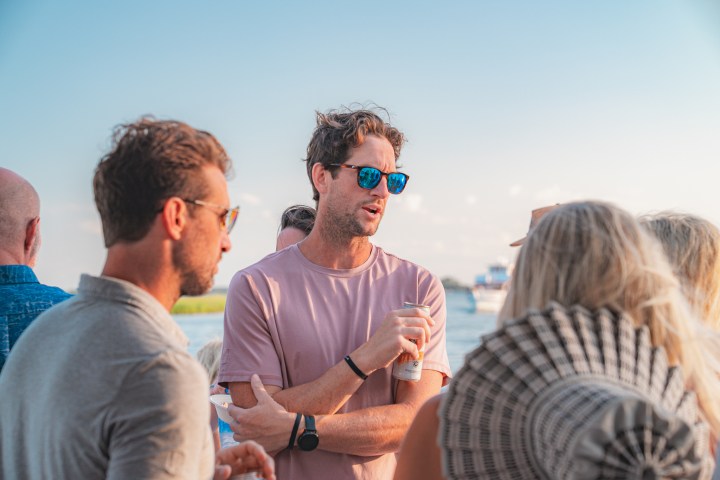 Group of people talking outdoors on a sunny day near water.