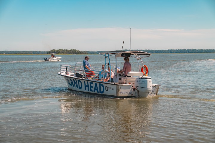 Small motorboat with people cruising on a lake under a clear sky.
