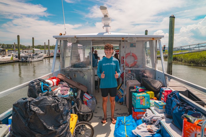 Person on a boat docked, surrounded by bags and supplies, smiling and giving thumbs up.