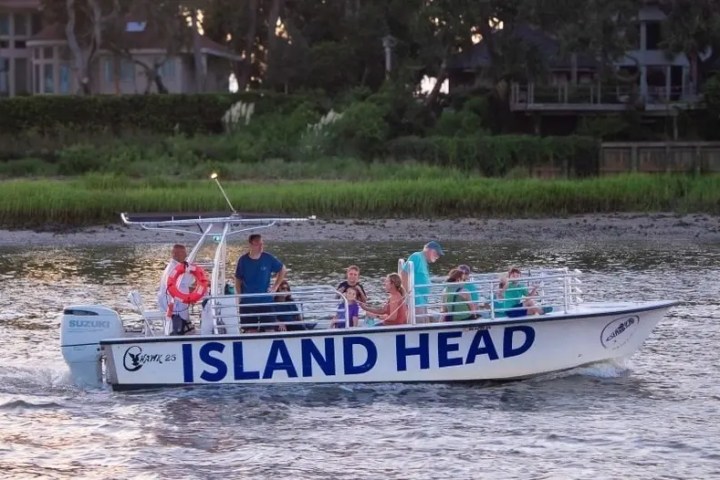 A group of people on a boat named 'ISLAND HEAD' cruising near the shoreline.
