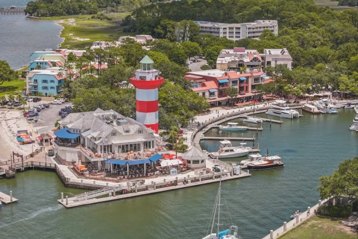 Aerial view of marina with red-striped lighthouse and boats docked.