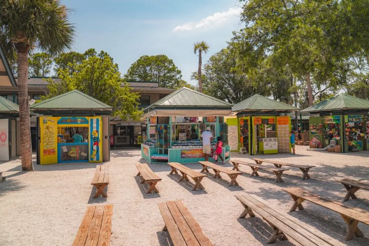 Outdoor market with colorful stalls and wooden benches under a sunny sky.