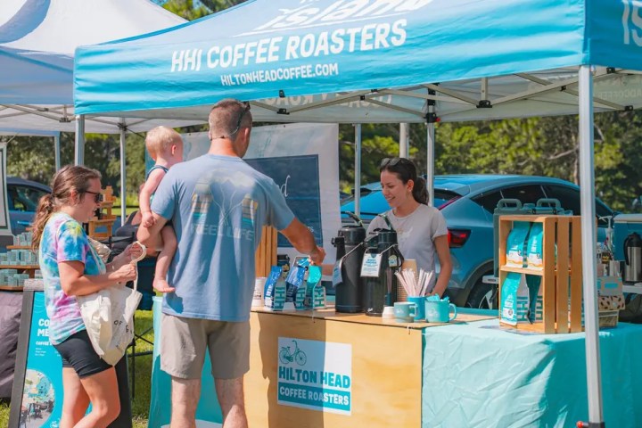 Family at coffee stall under a blue tent at an outdoor market.